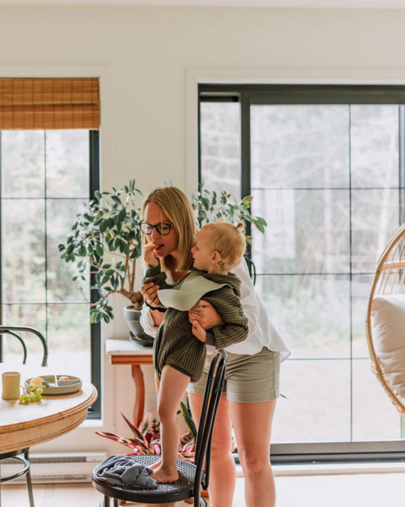 Maman et enfant jouant à table avec bavette en silicone couleur grège.