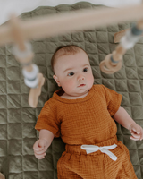 Bébé sur le dos sur tapis matelassé rond couleur sauge.