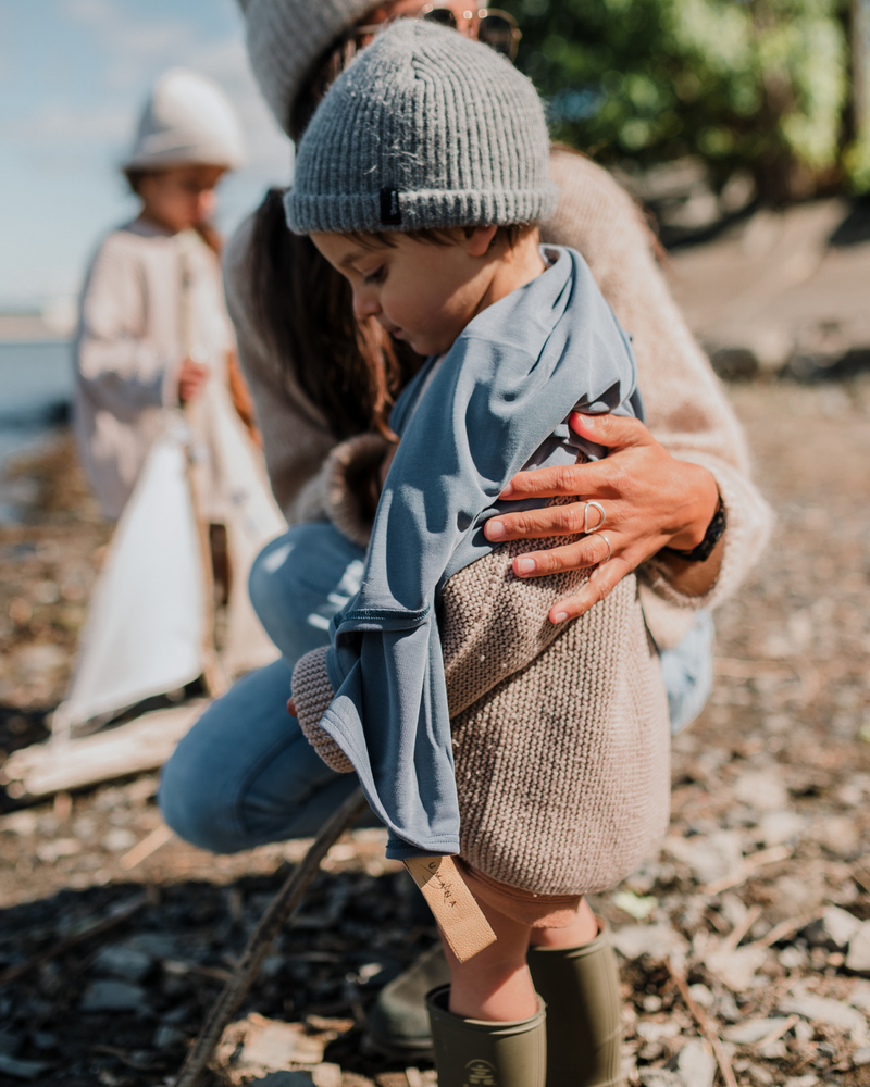 Maman tenant enfant sur la plage avec doudou douce bleu profond.