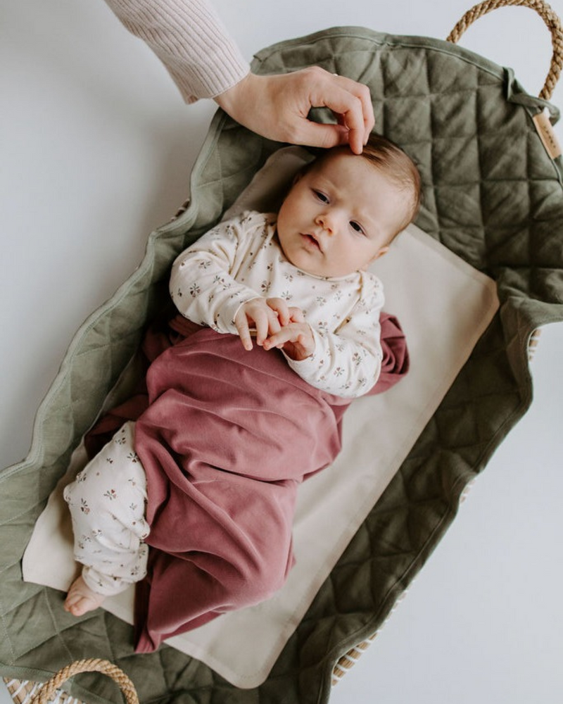 Tapis à langer couleur sauge dans un panier à langer avec bébé et main de maman.